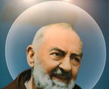 São Padre Pio de Pietrelcina com as mãos cobertas por luvas (devido aos estigmas), segurando um terço e sorrindo serenamente